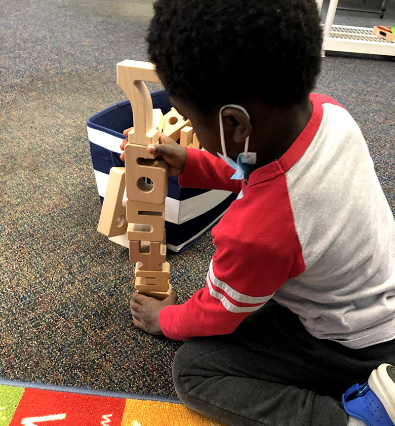 Young African American boy explores early childhood development through play with wooden building blocks in a nurturing preschool environment.