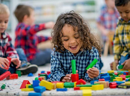 A young boy with long hair engages in playful learning with colorful blocks, fostering early childhood development in a nurturing preschool setting.